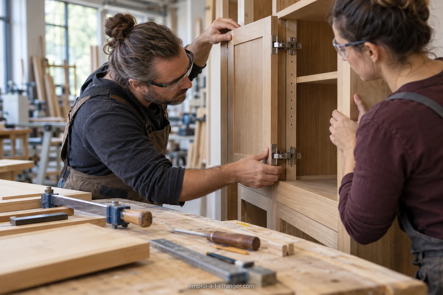 Menuisier et collègue ajustant la porte d’un meuble en bois dans leur atelier.